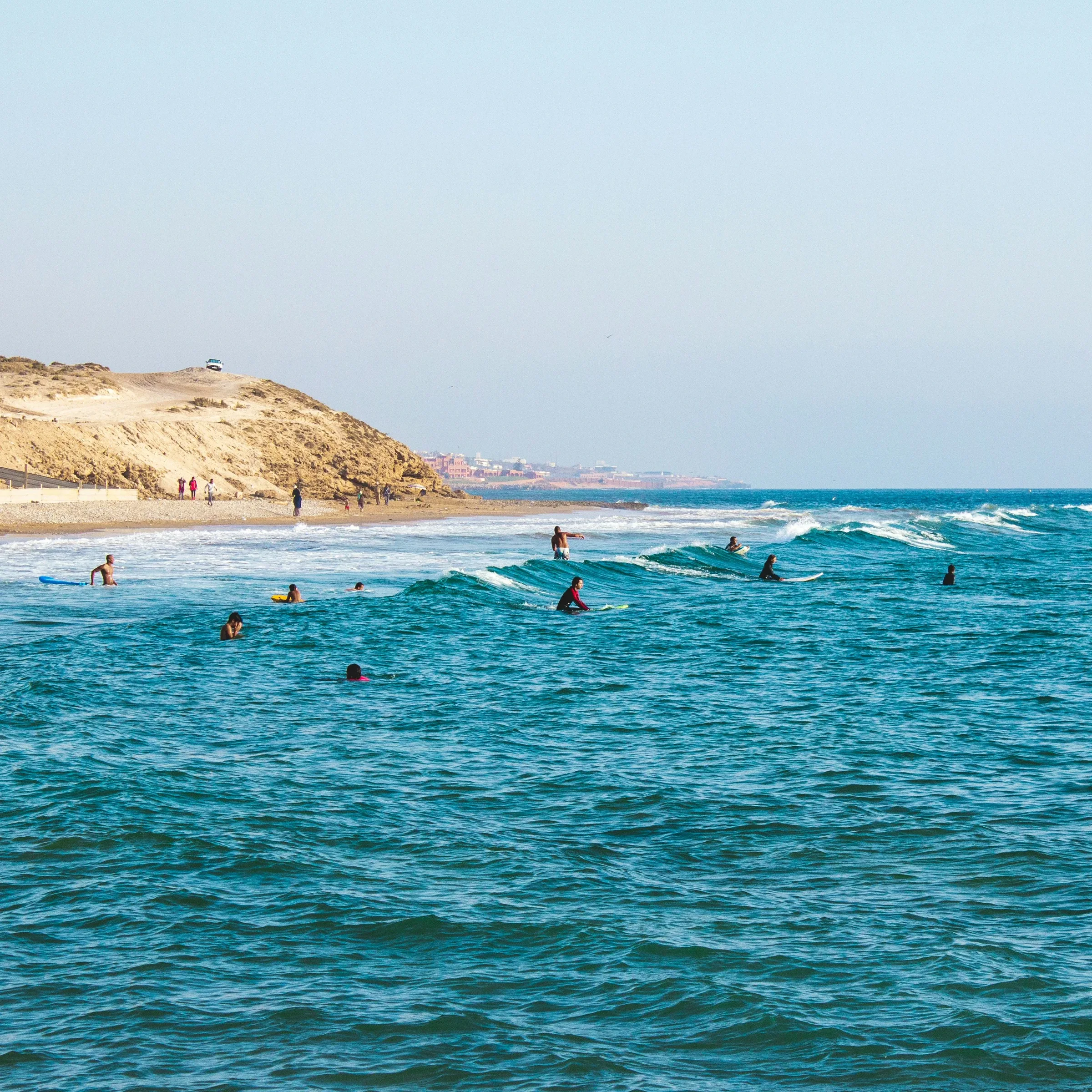Surfers in blue water by the Tamraght coast, Morocco — صورة حقيقية للمنطقة، وليست صورة لأماكن إقامة المخيم